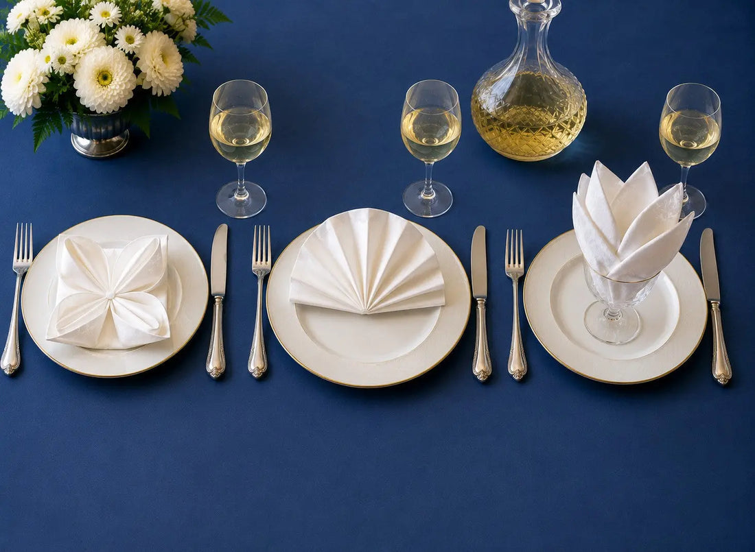 Trois pliages de serviettes en tissu élégants sur table dressée : nénuphar, éventail et pétales dans un verre