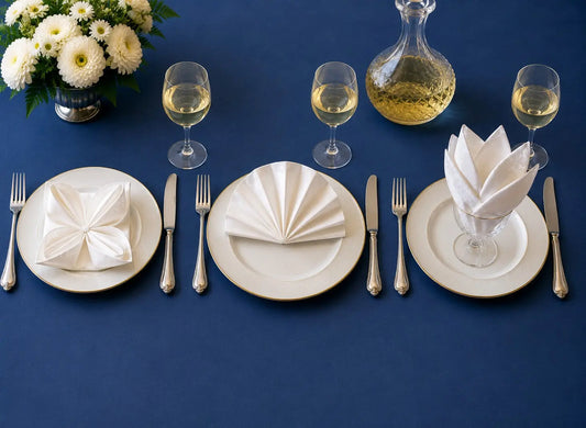Trois pliages de serviettes en tissu élégants sur table dressée : nénuphar, éventail et pétales dans un verre
