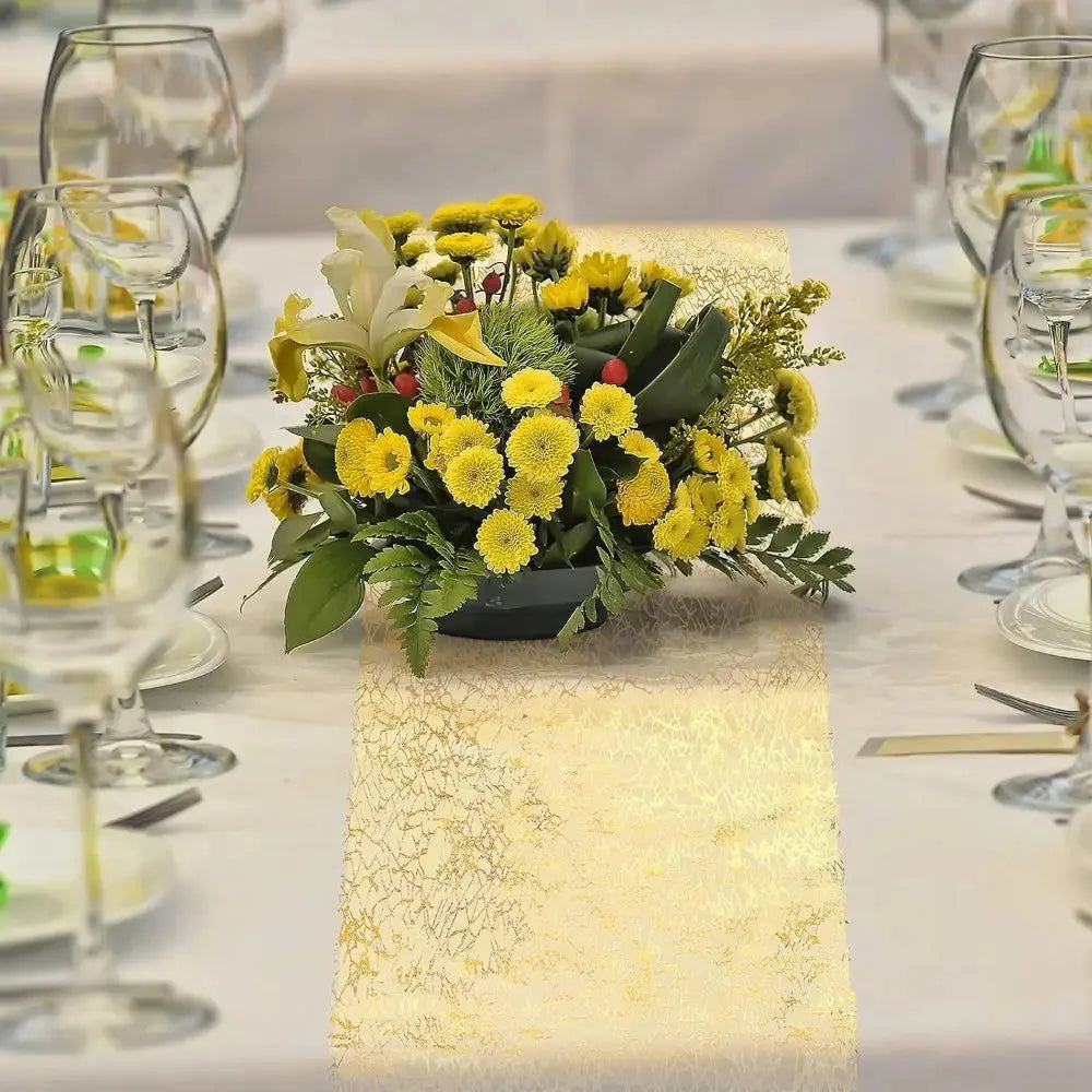 Image d'un superbe chemin de table doré au style métallique sur une nappe blanche ornée de multiples verres à vin ainsi qu'un étincelant bouquet de petites fleurs jaunes