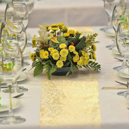 Image d'un superbe chemin de table doré au style métallique sur une nappe blanche ornée de multiples verres à vin ainsi qu'un étincelant bouquet de petites fleurs jaunes