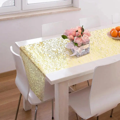 Image d'un superbe chemin de table doré au style métallique sur une jolie table en bois blanc accompagné d'un  magnifique pot de roses 
