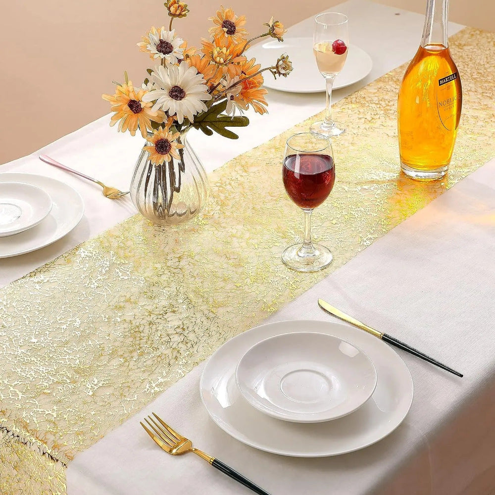 Image d'un chemin de table doré au style métallique sur une table ornée d'un nappe blanche avec un joli pot de fleurs et une coupe de vin