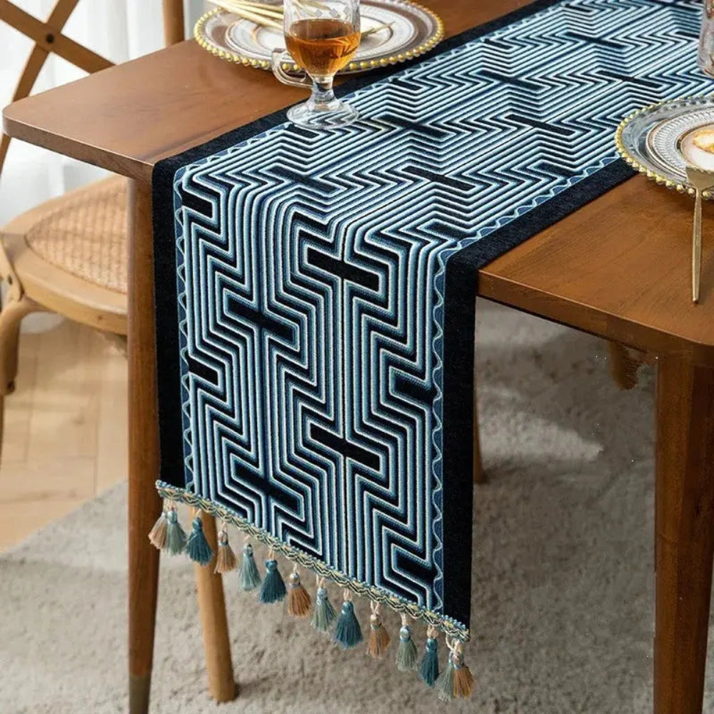 Image d'un chemin de table jacquard aux formes géométriques bleu et noir  vu de près avec de jolis pompons sur une table en bois