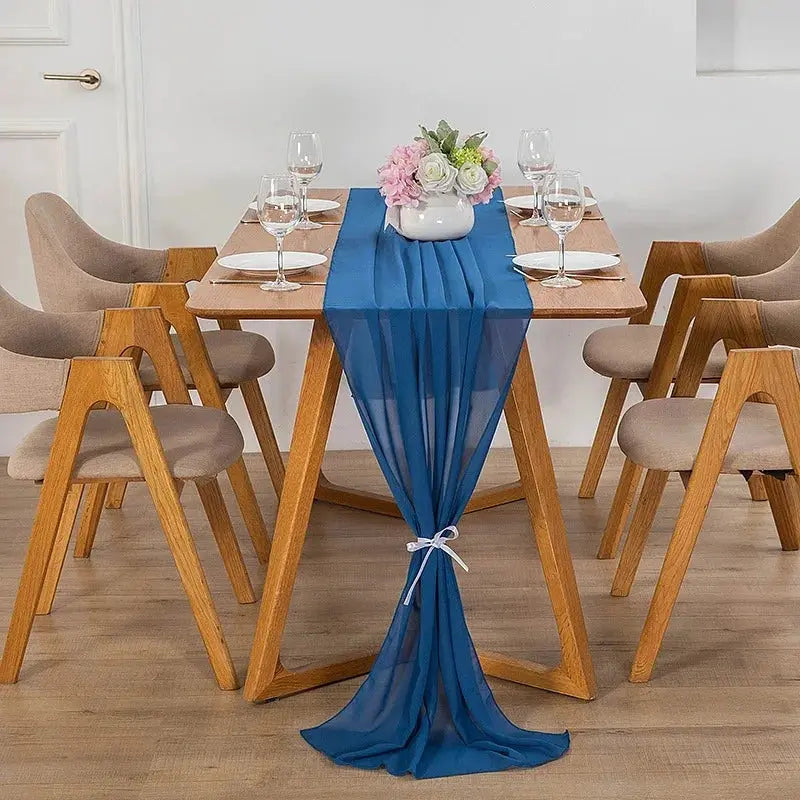 Image d'un chemin de table en mousseline bleu sur une jolie table en bois ornée d'un beau bouquet de fleurs