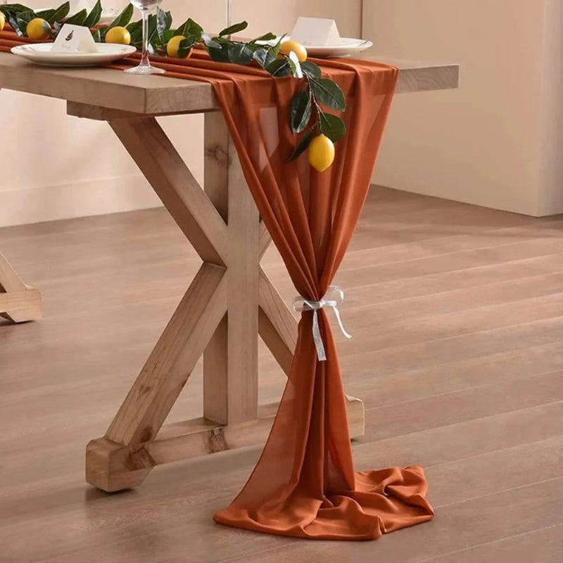 Image d'un chemin de table en mousseline orange sur une jolie table en bois décorée d'une branche avec des citrons
