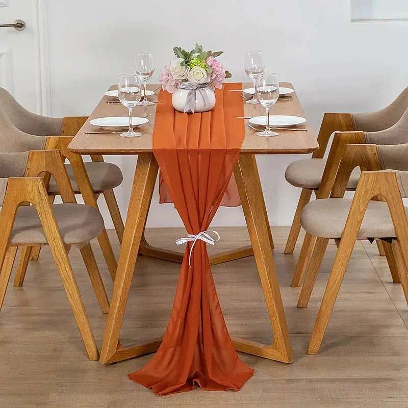 Image d'un chemin de table en mousseline orange sur une jolie table en bois ornée d'un beau bouquet de fleurs