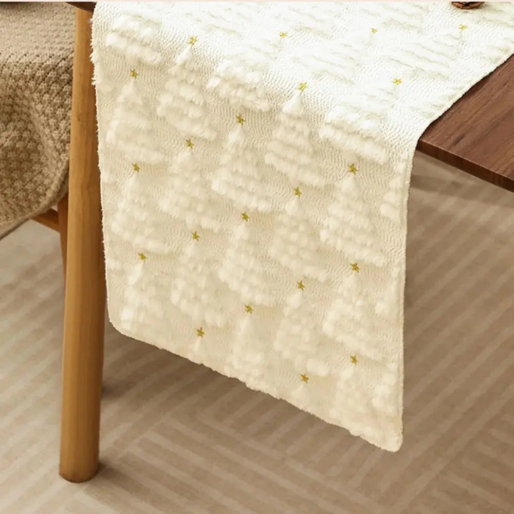 Élégant et doux chemin de table de Noël de couleur blanche crème avec de petits sapins tissés en relief, placé sur une table en bois, vu de très près