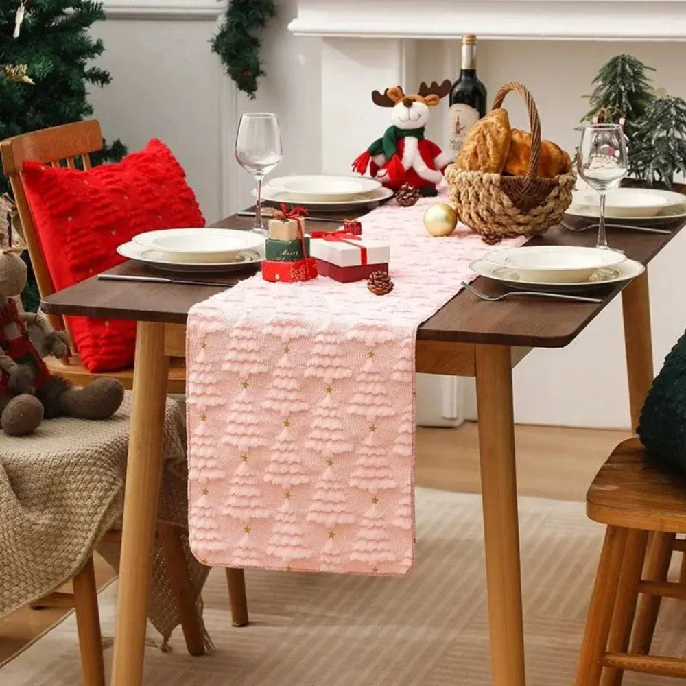 Élégant et doux chemin de table de Noël de couleur rose avec de petits sapins tissés en relief, placé sur une jolie table à dîner en bois au décor des Fêtes
