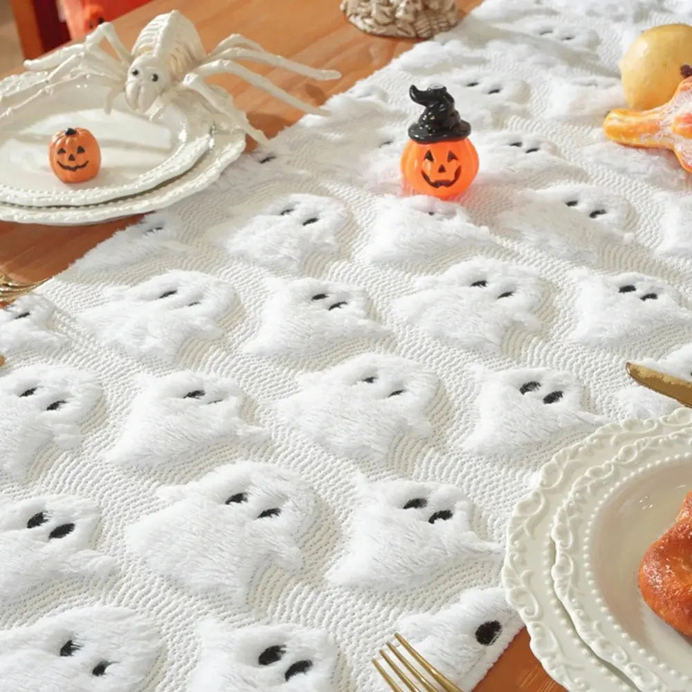 Image d'un chemin de table blanc brodé de petits fantômes accompagné de quelques citrouilles et d'une grosse araignée décoratives
