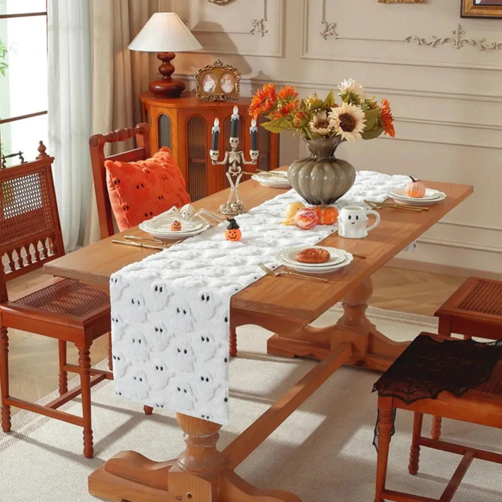 Image d'un chemin de table blanc brodé de petits fantômes sur une table en bois dur décorée avec un joli pot de fleurs et un chandelier en forme de squelette
