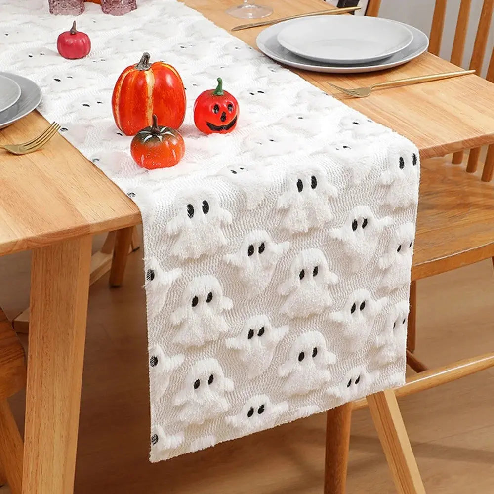 Image d'un chemin de table blanc brodé de petits fantômes sur une table en bois dur ornée de décorations en forme de citrouilles