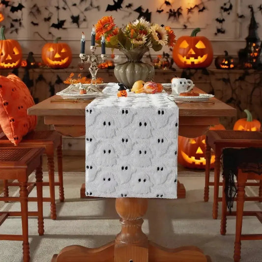 Image d'un chemin de table blanc brodé de petits fantômes sur une table en bois avec de multiples citrouilles décorées en arrière-plan