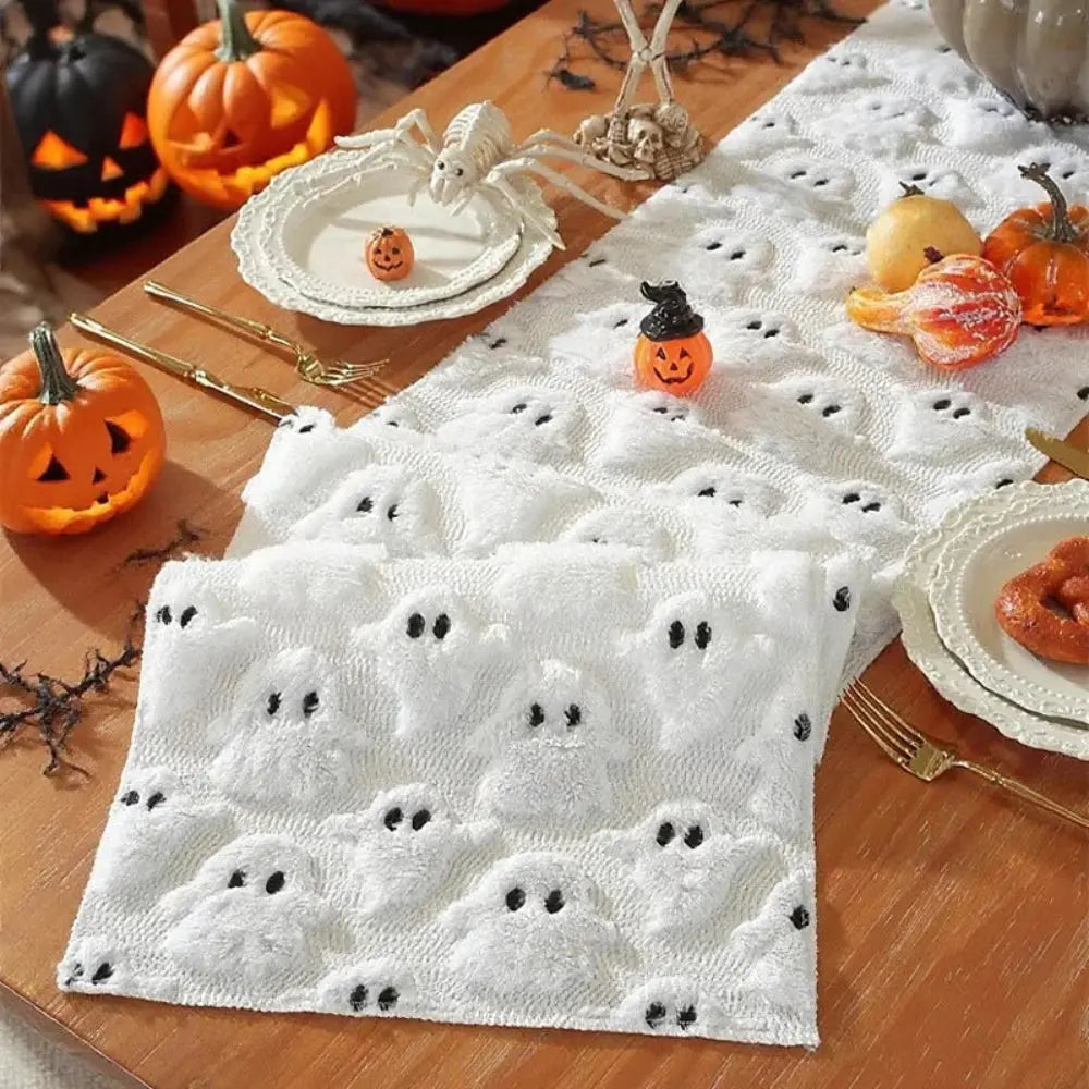 Image d'un chemin de table blanc brodé de petits fantômes placé en accordéon sur une table en bois dur ornée de mignonnes citrouilles décoratives