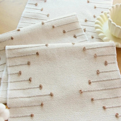 Image d'un chemin de table de couleur crème en coton replié sur lui-même avec ses jolis motifs tissés en couleur 