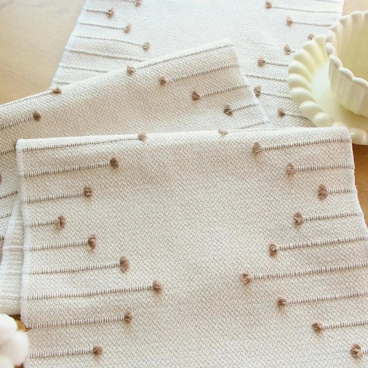 Image d'un chemin de table de couleur crème en coton replié sur lui-même avec ses jolis motifs tissés en couleur 