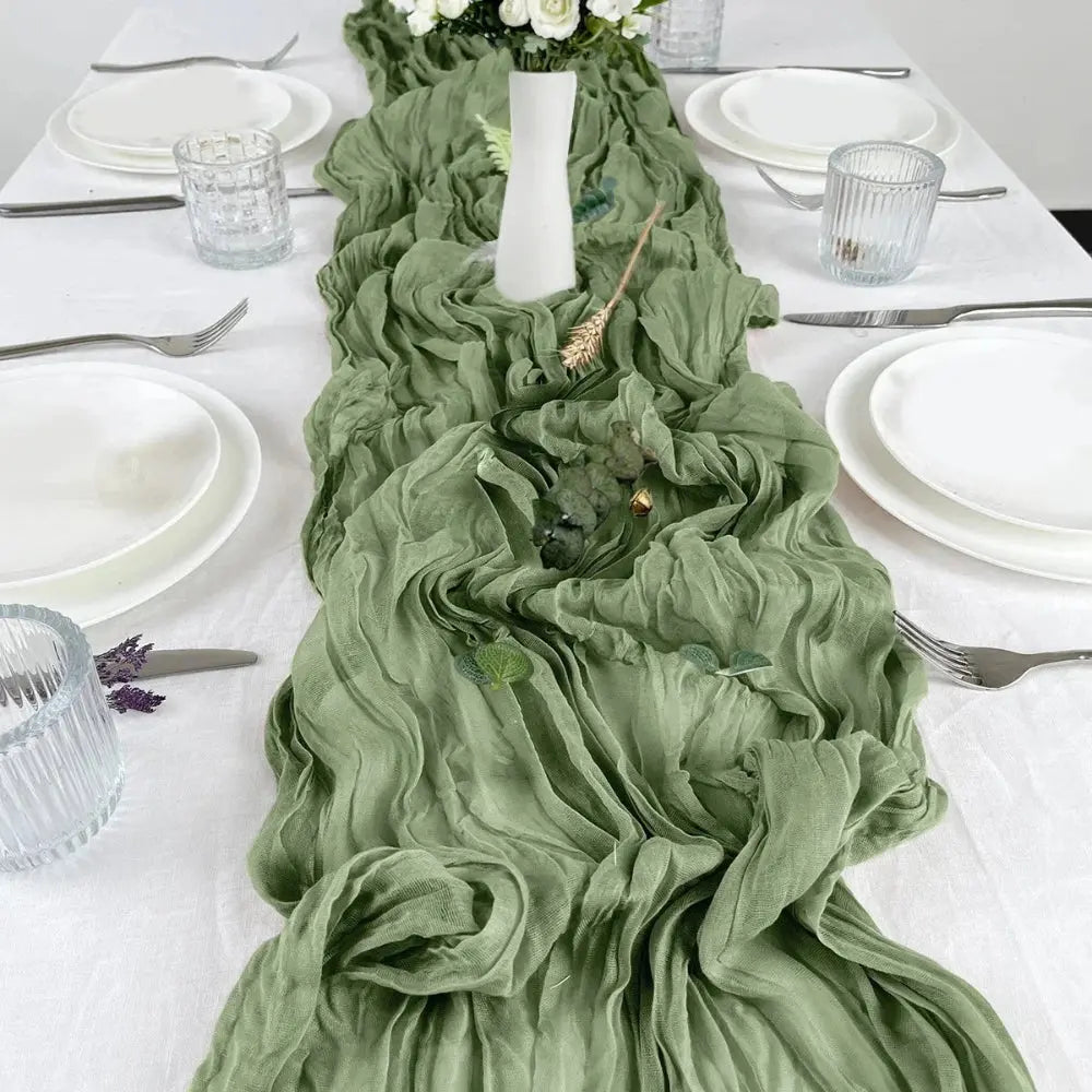Image d'un chemin de table vert sauge sur une jolie table ornée d'une vaisselle blanche pure