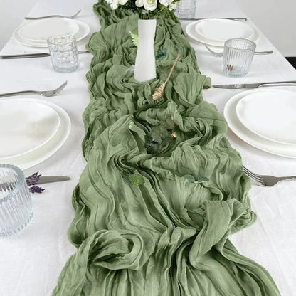 Image d'un chemin de table vert sauge sur une jolie table ornée d'une vaisselle blanche pure