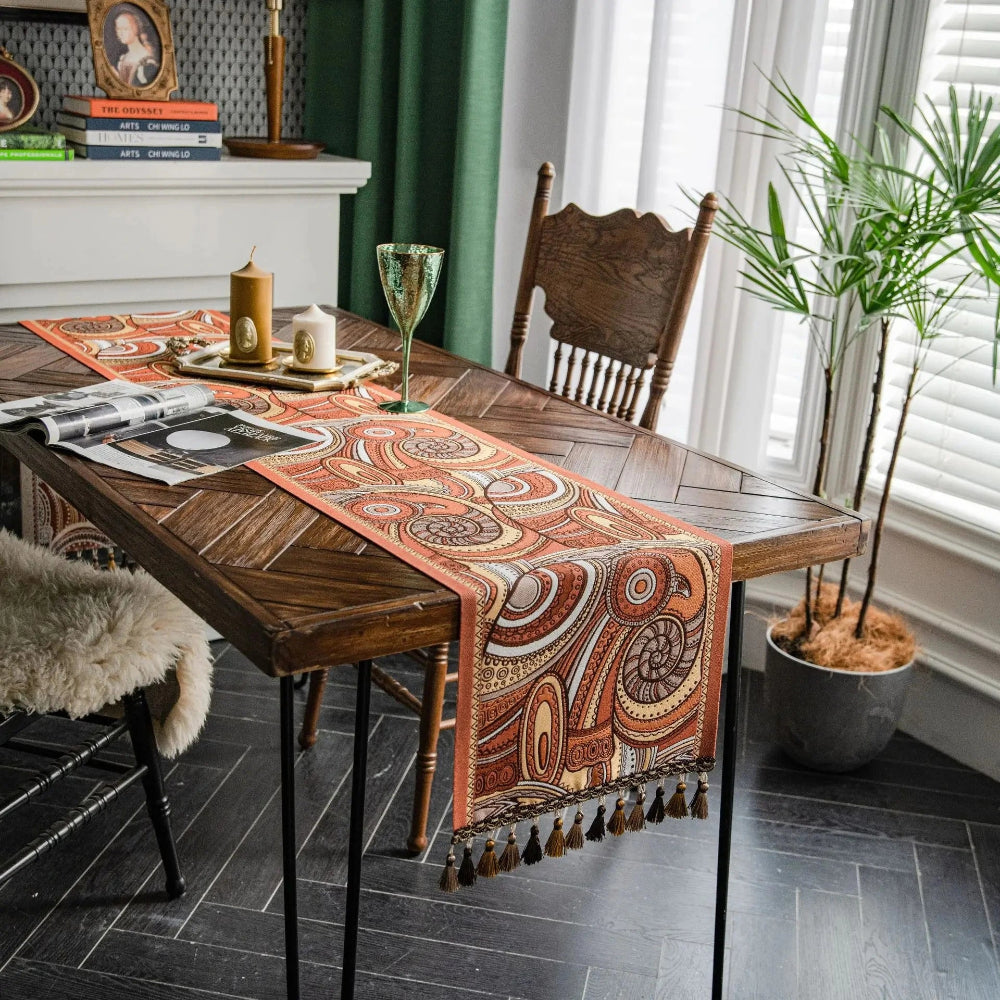 Image d'un magnifique et coloré chemin de table de style vintage avec un motif colimaçon et autres formes abstraites placé sur une belle table en bois accompagné de bougeoirs, d'un verre à vin et d'un magazine