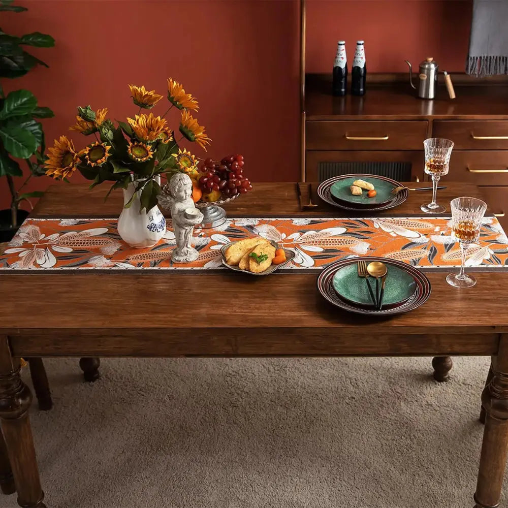 Image d'un magnifique et coloré chemin de table de style vintage avec un motif épi placé sur une belle table en bois accompagné de deux couverts, deux verres de vin et d'un joli bouquet de tournesols dans un vase