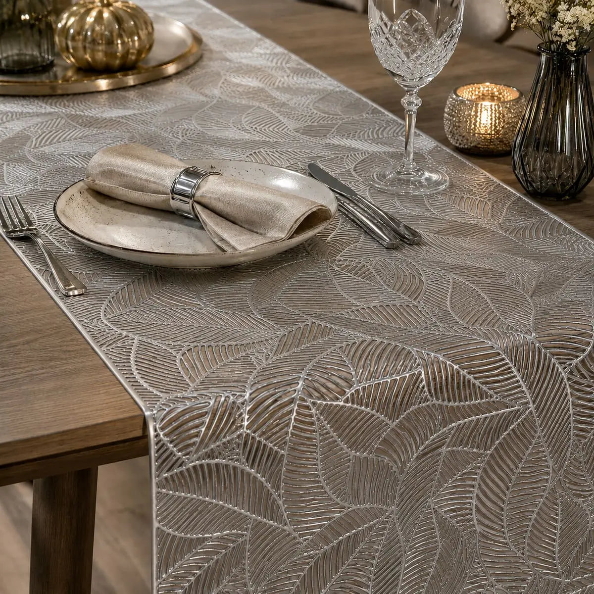 Gros plan sur le motif de feuille ajouré du chemin de table vinyle argenté, décoration d'automne avec citrouilles dorées