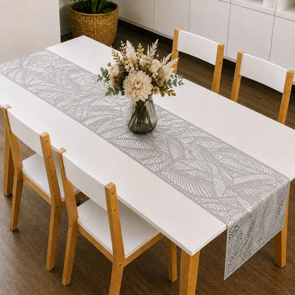 Chemin de table vinyle argenté au motif de feuille sur table à manger blanche, avec bouquet de fleurs séchées