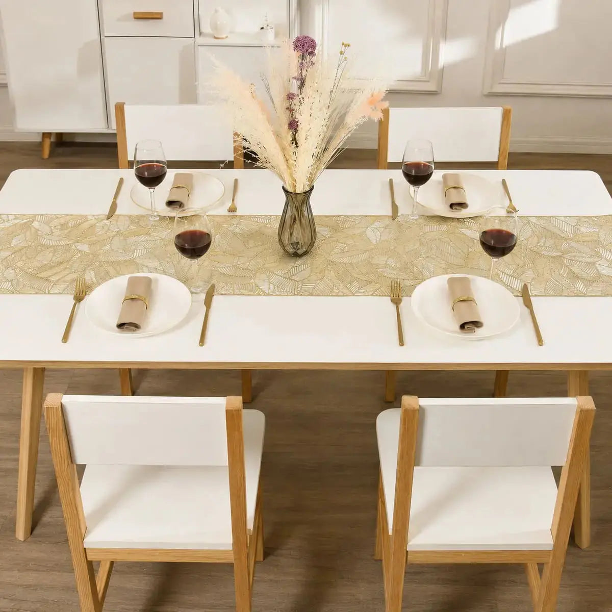 Chemin de table vinyle doré au motif de feuille sur une table à dîner dressée pour quatre, avec verres à vin et fleurs séchées