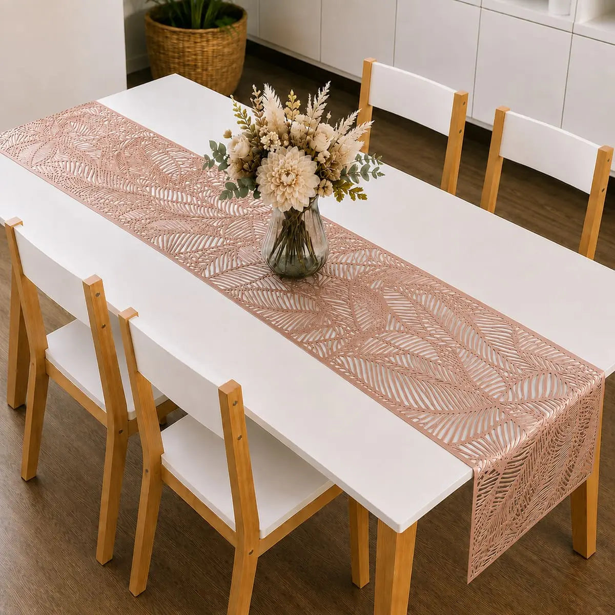 Chemin de table vinyle rose doré au motif de feuille sur table à manger blanche, avec bouquet de fleurs séchées