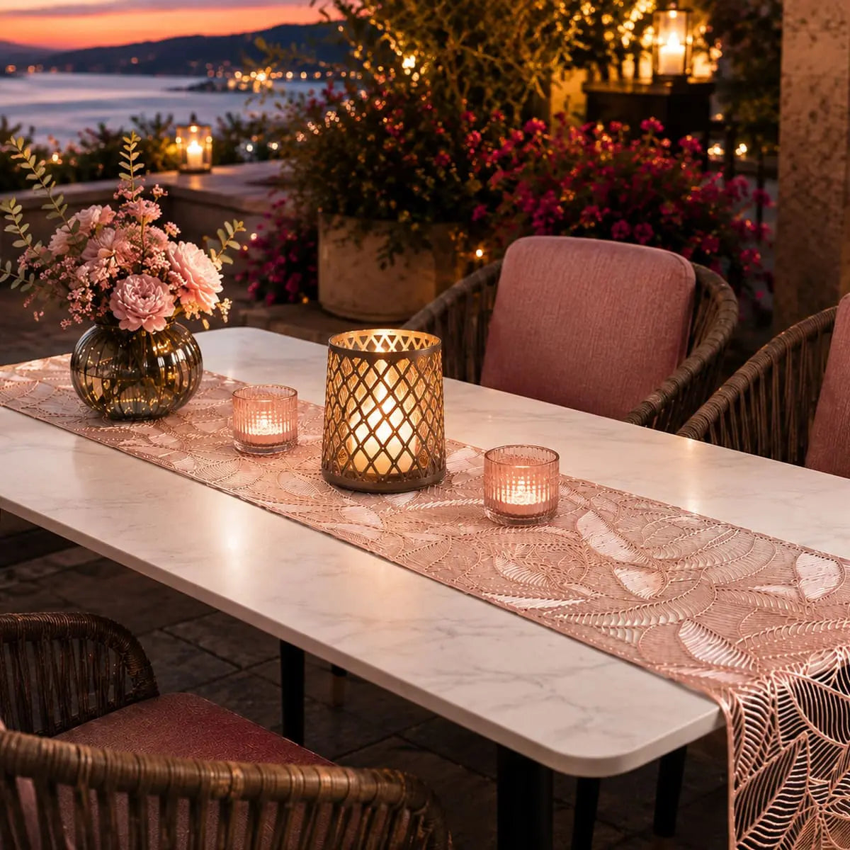Chemin de table rose doré au motif feuille sur table en marbre, terrasse au coucher du soleil avec bougies et fleurs roses