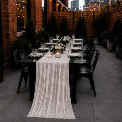 Chemin de table voilage plissé blanc sur table dressée en terrasse extérieure, avec guirlandes lumineuses et bouquet de roses