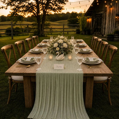 Chemin de table voilage plissé vert sauge sur table de baptême en extérieur avec bouquet de roses blanches et cygne décoratif