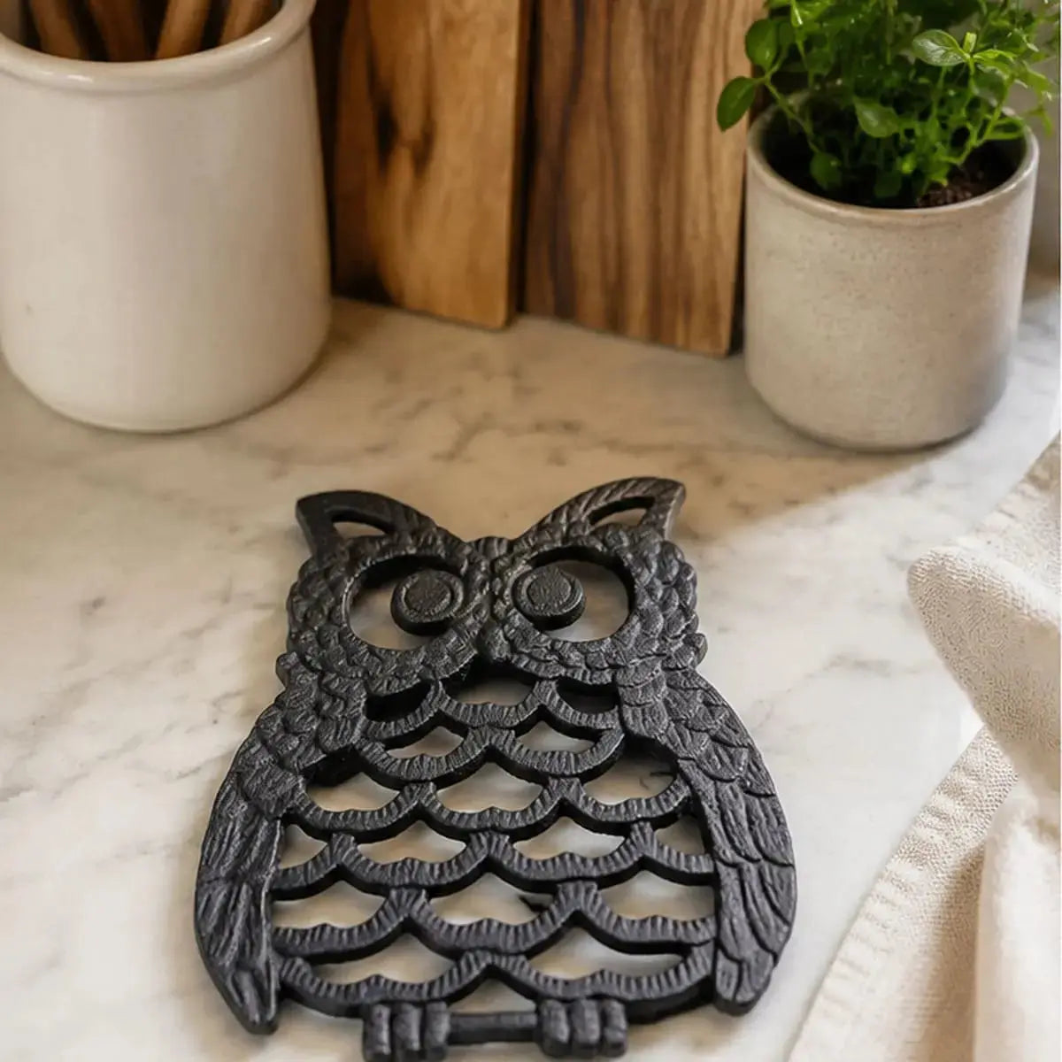 Gros plan sur le dessous de plat en fonte en forme de hibou noir posé sur un comptoir en marbre entouré de plantes