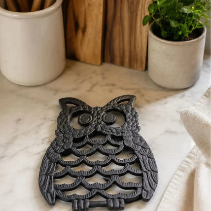 Gros plan sur le dessous de plat en fonte en forme de hibou noir posé sur un comptoir en marbre entouré de plantes