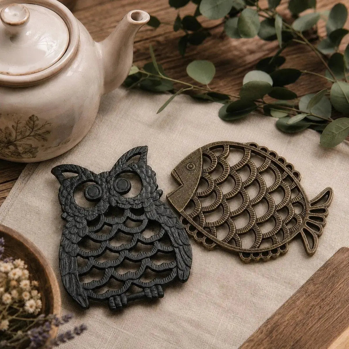Dessous de plat en fonte en forme de hibou noir et de poisson cuivré posés côte à côte près d'une théière en céramique