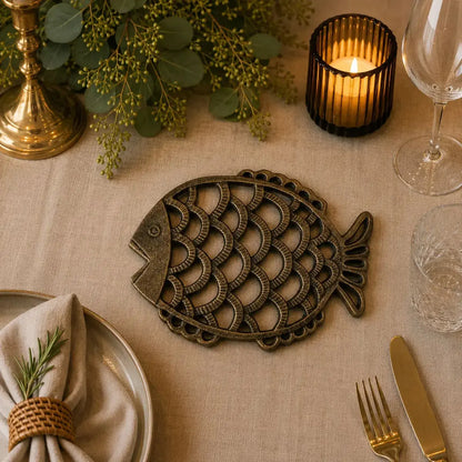 Dessous de plat en fonte en forme de poisson cuivré sur une table dressée avec bougie et verres