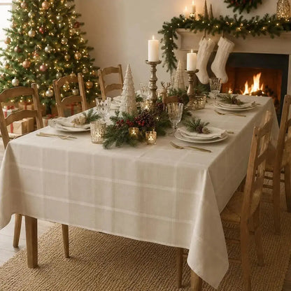 Nappe de table beige à carreaux dressée pour Noël devant une cheminée allumée, avec bas de Noël et sapin décoré