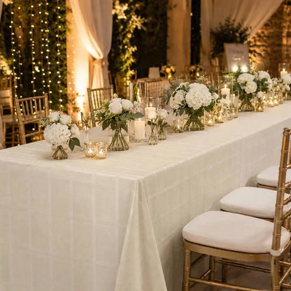Nappe de table beige habillant une longue table de réception de mariage avec fleurs blanches et bougies