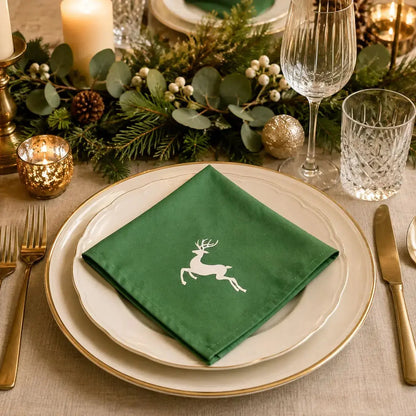 Gros plan sur une serviette de table de Noël en coton vert à motif renne, posée sur assiette dorée